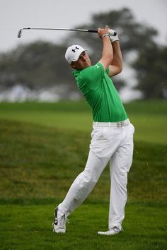 a man in green shirt and white pants playing golf