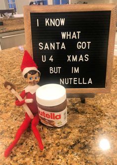 an elf is sitting next to a sign that says i know what santa got u4 xmas but im nutella