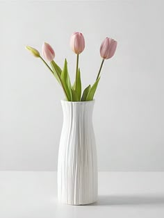 a white vase filled with pink flowers on top of a table