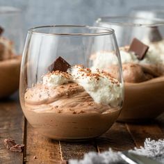 two glasses filled with dessert sitting on top of a wooden table