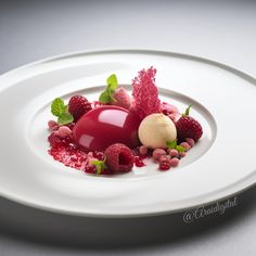 a white plate topped with raspberry dessert and garnished with mint leaves