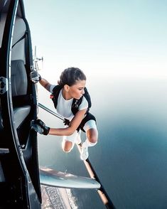 a woman in white shirt and black shorts hanging off the side of an airplane window