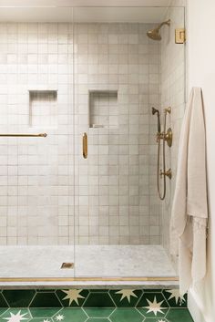 a bathroom with green and white tiles on the floor, shower stall door and towel rack