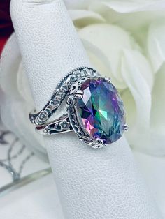 Simulated Mystic Topaz Ring Set Edward Design#70 Made To Order This filigree ring is an Edwardian antique reproduction in sterling silver set with a 6 carat simulated Rainbow Mystic Topaz gemstone solitaire. This faceted cut oval gem is 14mm x 10mm. This ring sits 7mm off the finger. The inside of the band is marked 925 for sterling silver. This ring now has a matching floral accompanying curved band. This band was specially designed to fit this ring perfect. You can elect to purchase just the r Mystic Topaz Ring, Vintage Style Rings, Purple Band, Mystic Topaz, Filigree Ring, Engraved Items, Lovely Jewellery, Silver Filigree, Topaz Gemstone