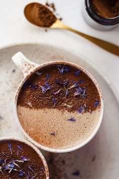 two mugs filled with hot chocolate and sprinkles on top of a white plate