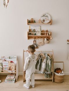 a little boy that is standing in front of a shelf with some clothes on it