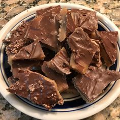 a white plate topped with chocolate pieces on top of a marble countertop next to a blue and white bowl