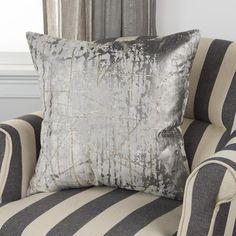 a silver and black pillow sitting on top of a striped chair next to a window