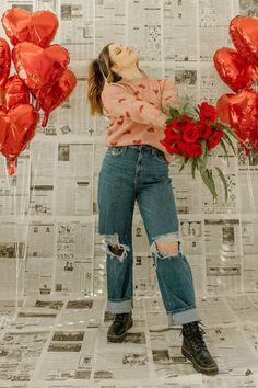 a woman standing in front of red balloons and flowers with her head tilted to the side