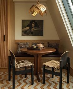 a table with two chairs and a painting on the wall above it in a small room