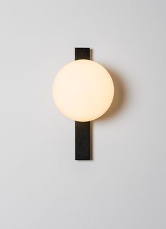 a wall light mounted on the side of a white wall next to a black pole