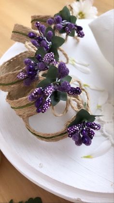 purple flowers are tied to twine and placed on top of a white plate with burlap