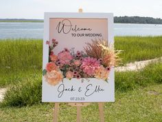 a welcome sign with flowers on it in front of the water and grass near a beach