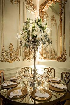 a fancy dining table with flowers and place settings in front of an ornate wall mirror