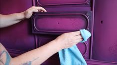 a woman is cleaning the purple cupboards with a blue towel and cloth in her hand