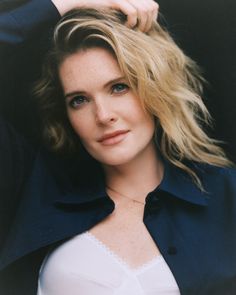 a close up of a person wearing a white shirt and blue jacket with her hand on her head