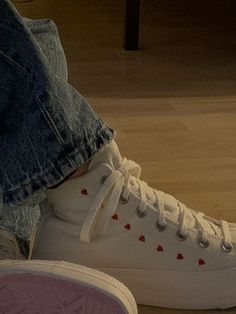 a person wearing white sneakers with red hearts on the soles and their shoes are next to each other