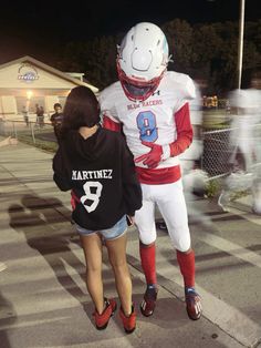 two people in football uniforms are walking down the street at night with one person dressed as a football player