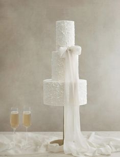 a three tiered wedding cake with two champagne glasses on the table next to it