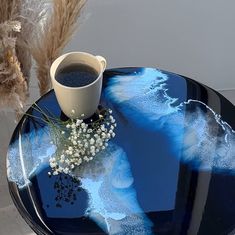 a blue glass table with a cup of coffee and some dried flowers on the side