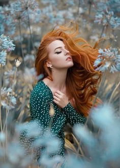 a woman with long red hair standing in blue flowers