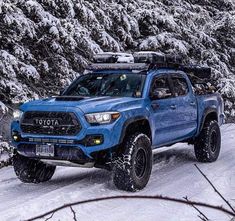 a blue truck driving down a snow covered road with skis on it's roof