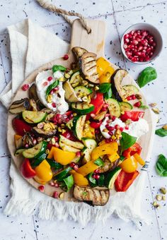 a wooden platter filled with grilled vegetables and pomegranates