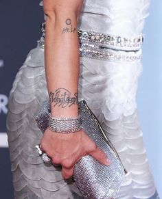 a woman with tattoos on her arm holding onto a silver purse and wearing a white dress