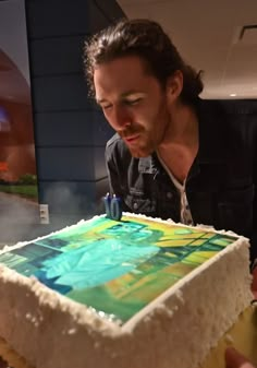 a man blowing out the candles on a cake that has been decorated with colorful images