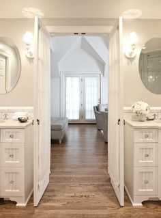 an open door leading to a living room with white furniture and mirrors on the wall