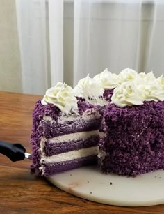 a slice is taken out of a purple cake with white frosting on the side