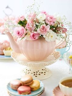 a pink tea pot filled with flowers on top of a table next to plates and cups