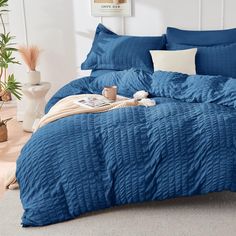 a bed with blue comforter and pillows in a room next to a potted plant