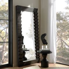 a large mirror sitting on top of a table next to a black vase and lamp