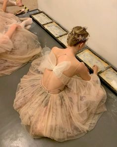 two women in dresses sitting on the floor with their backs turned to one another and looking at mirrors behind them