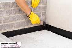 a person in yellow gloves and rubber gloves working on a cinder block wall with cement