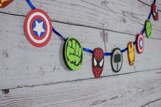 some paper cutouts are hanging from a string on a wooden planked wall, decorated with avengers and spider - man magnets