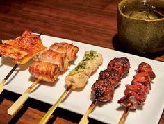 several skewers of food on a white plate with chopsticks next to it