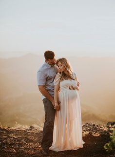 a pregnant couple standing on top of a mountain