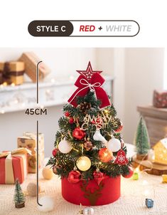 a small christmas tree in a red box on a table with presents and lights around it