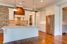 a large kitchen with white cabinets and wood flooring is pictured in this image, there are lights hanging from the ceiling over the island