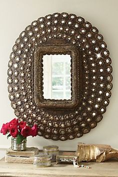 a round mirror sitting on top of a table next to a vase filled with flowers