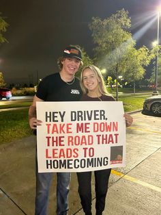 a man and woman holding a sign that says hey driver take me down the road that leads to home coming