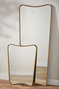 two mirrors sitting next to each other on top of a wooden floor in front of a white wall