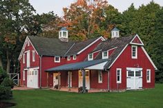 a large red barn with two white doors and windows on the front, surrounded by trees