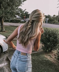 a woman standing in front of a car talking on a cell phone with her back to the camera