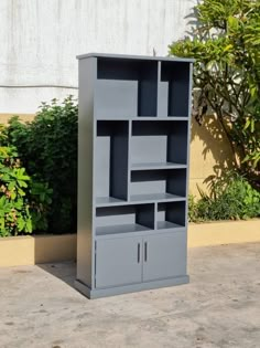 a gray bookcase sitting on top of a cement floor next to a planter