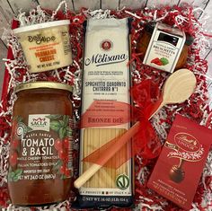 an open box containing pasta, tomato sauce and other condiments with wooden utensils