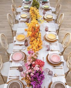 a long table is set with plates, flowers and napkins for an elegant dinner