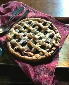 a pie sitting on top of a wooden table next to a knife and spoons